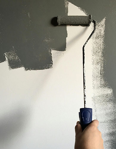 A person painting a wall with a roller, focused on applying a fresh coat of paint.